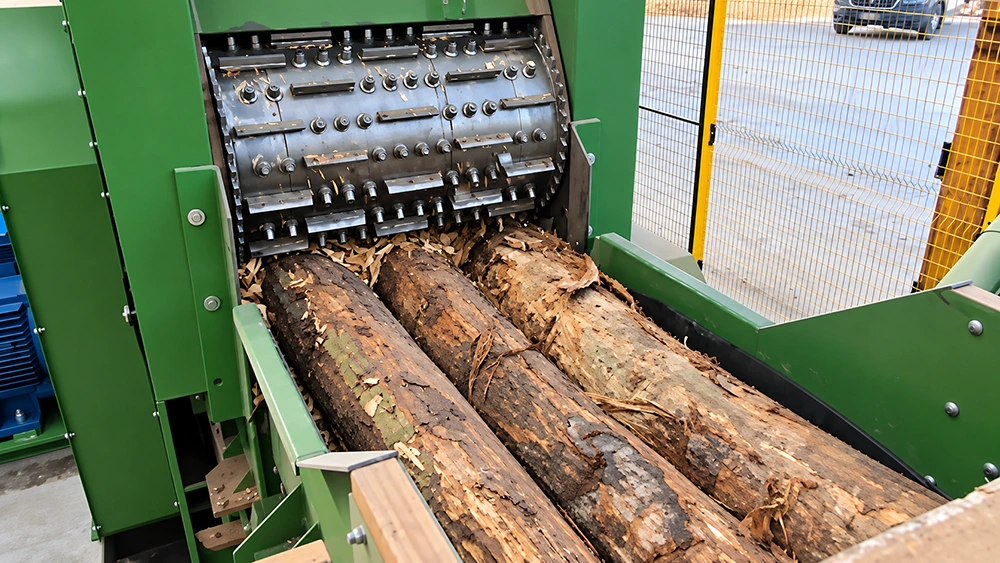 BX215 wood chipper drum cutter rotor feeding three bark-covered logs through a guarded feed chute for binder-free pellet plant chip prep
