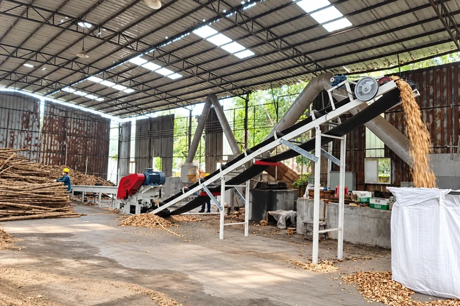 Industrial wood chipper line with inclined belt conveyor, ducting, and bulk bag discharge for biomass processing