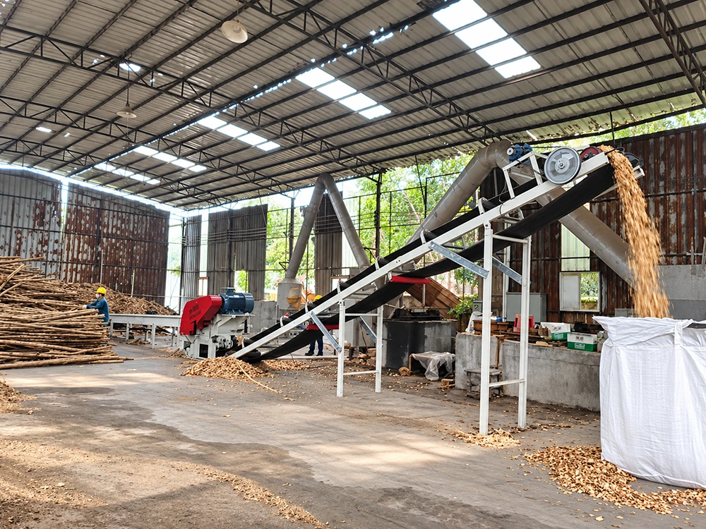 Industrial wood chipper line with inclined belt conveyor, ducting, and bulk bag discharge for biomass processing