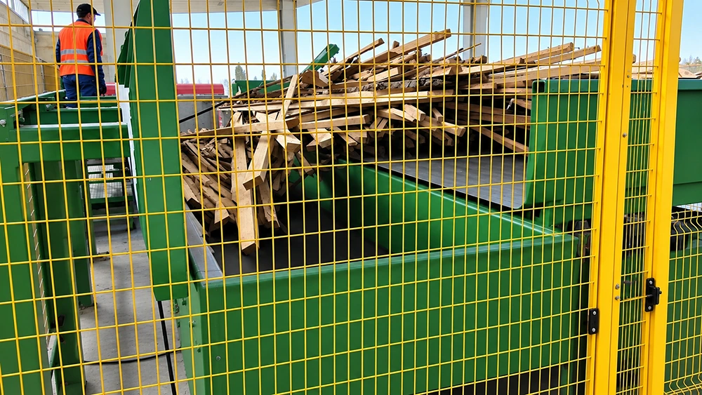 Electric wood chipper feed hopper receiving timber load at a wood recycling yard with operator platform