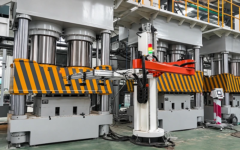 Multi-column hydraulic press station with striped safety guards and robotic transfer arm in factory