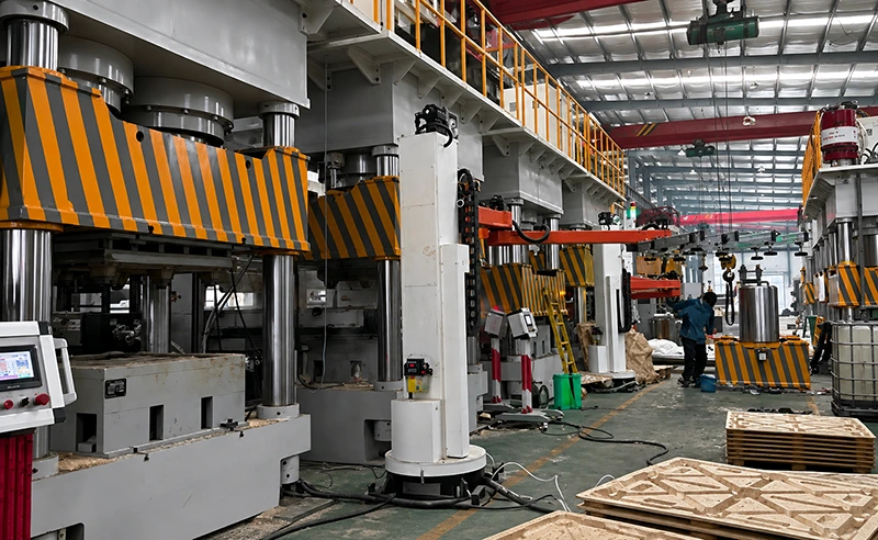Heavy-duty four-column hydraulic press in factory assembly hall with striped safety guards and overhead crane