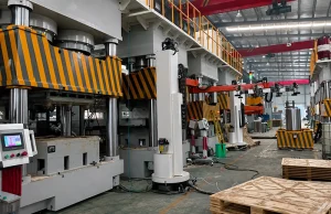 Factory-floor photo of a four-column hydraulic press with safety guards and robotic loading arm