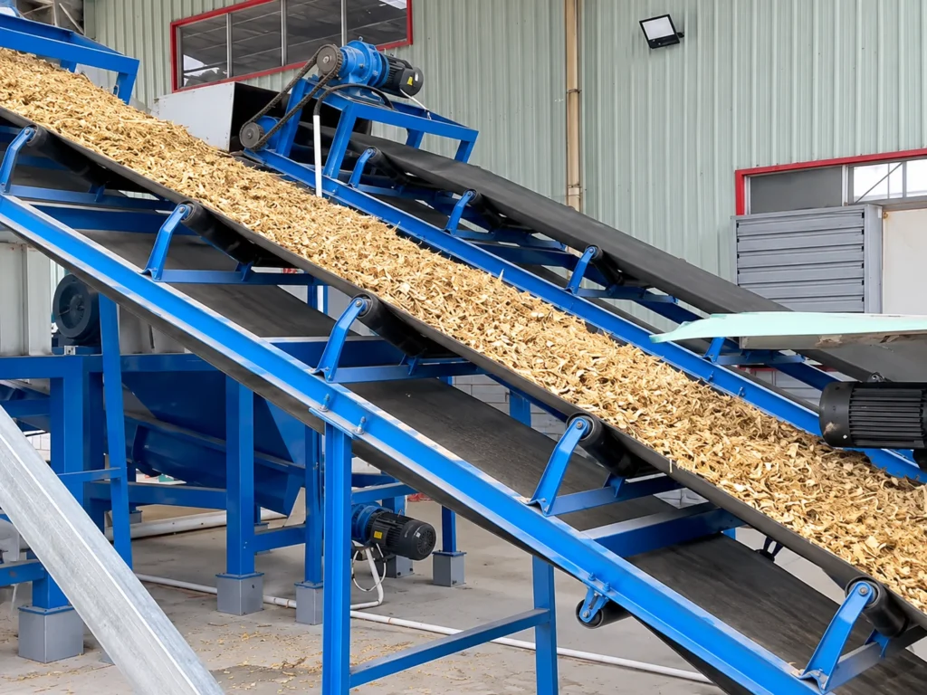 Wood pulverizer machine inclined belt conveyor carrying crushed wood chips to be graded by screen size in a presswood pallet line